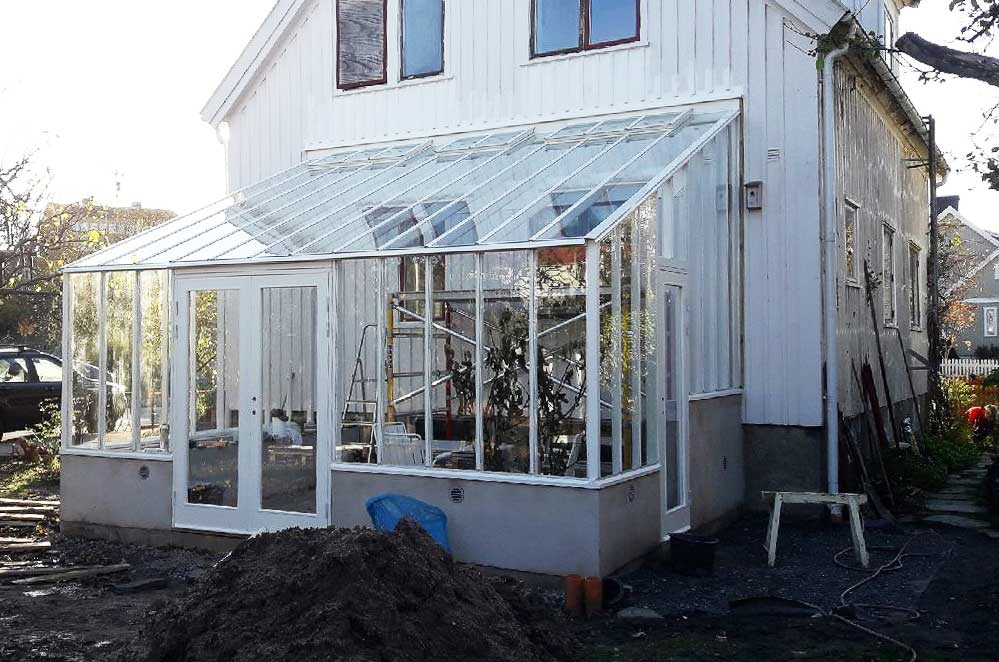 Svart växthus byggt mot stenhus.