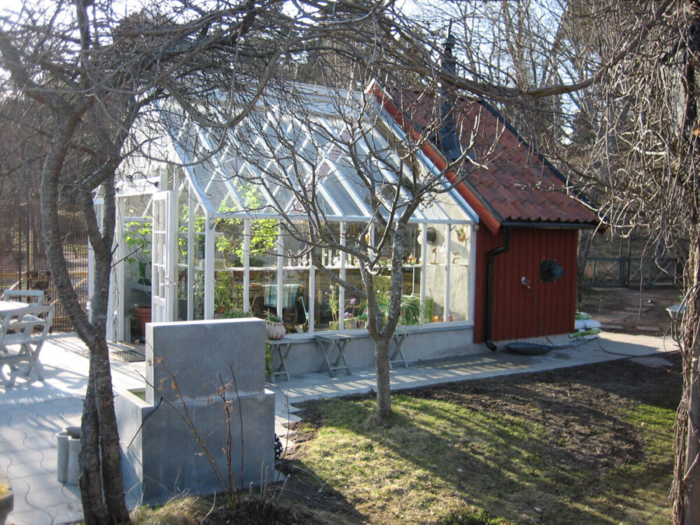 Växthus byggt mot rött förråd.