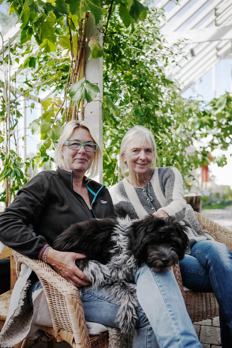 Två kvinnor och en hund sitter i växthuset