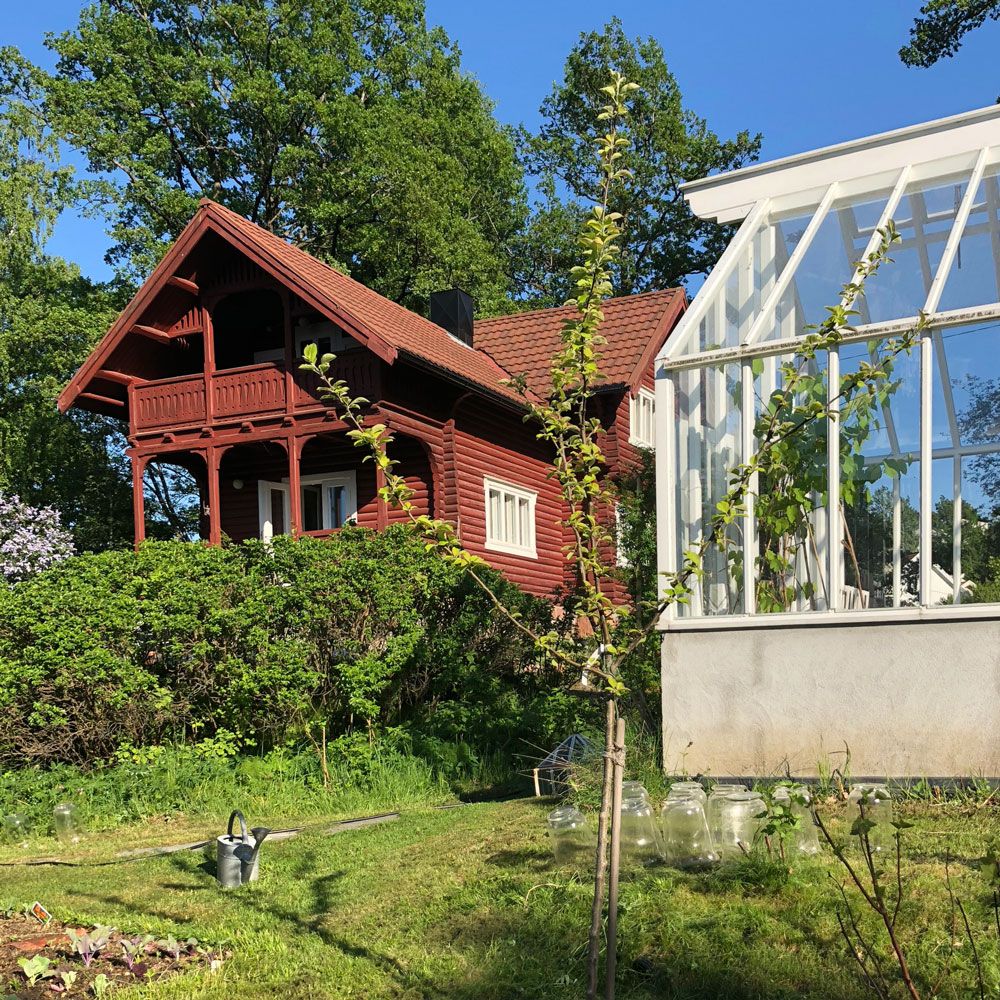 Rött bostadshus i drakstil bakom växthus.