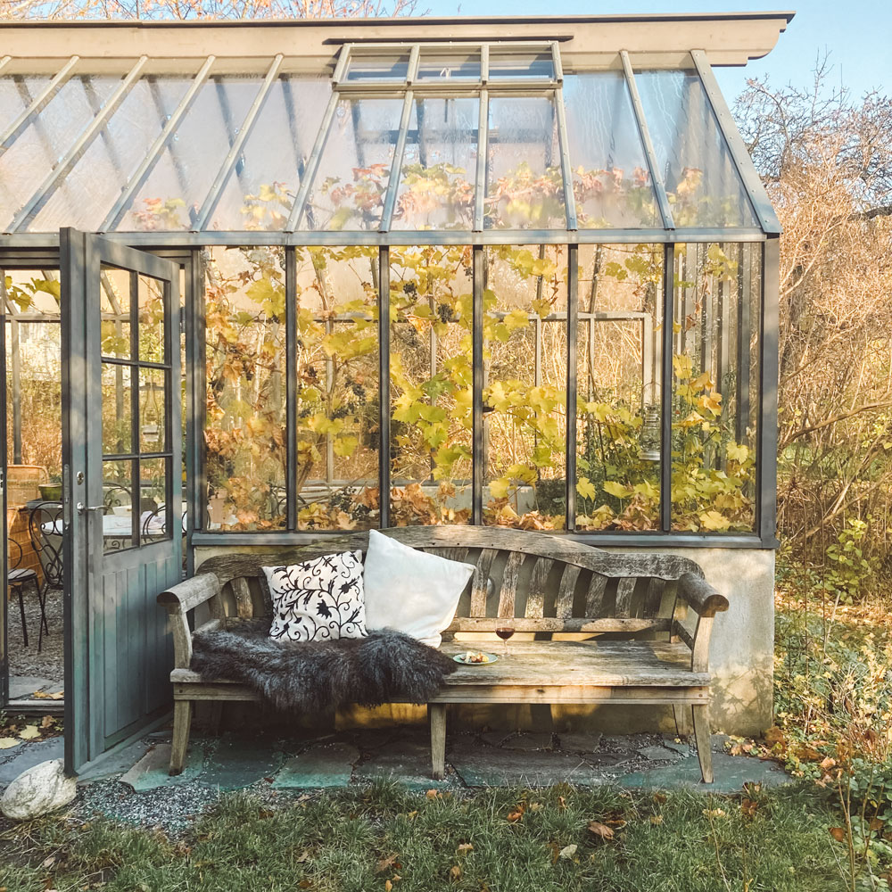 Träsoffa framför växthus.